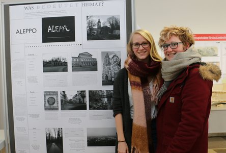 Studierende neben dem Plakat zum Thema Heimat