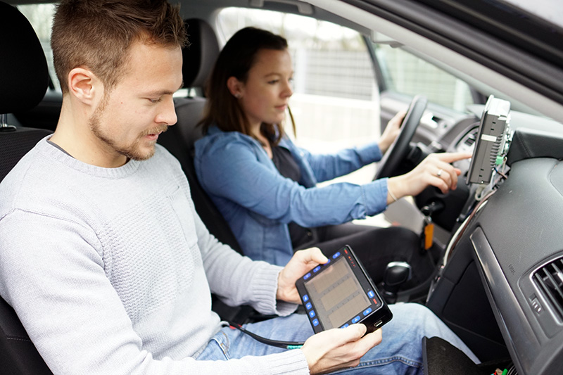 Ein Student und eine Studentin sitzen in einem Auto und testen eine Fahrzeug-Software, die sie selbst entwickelt haben. 